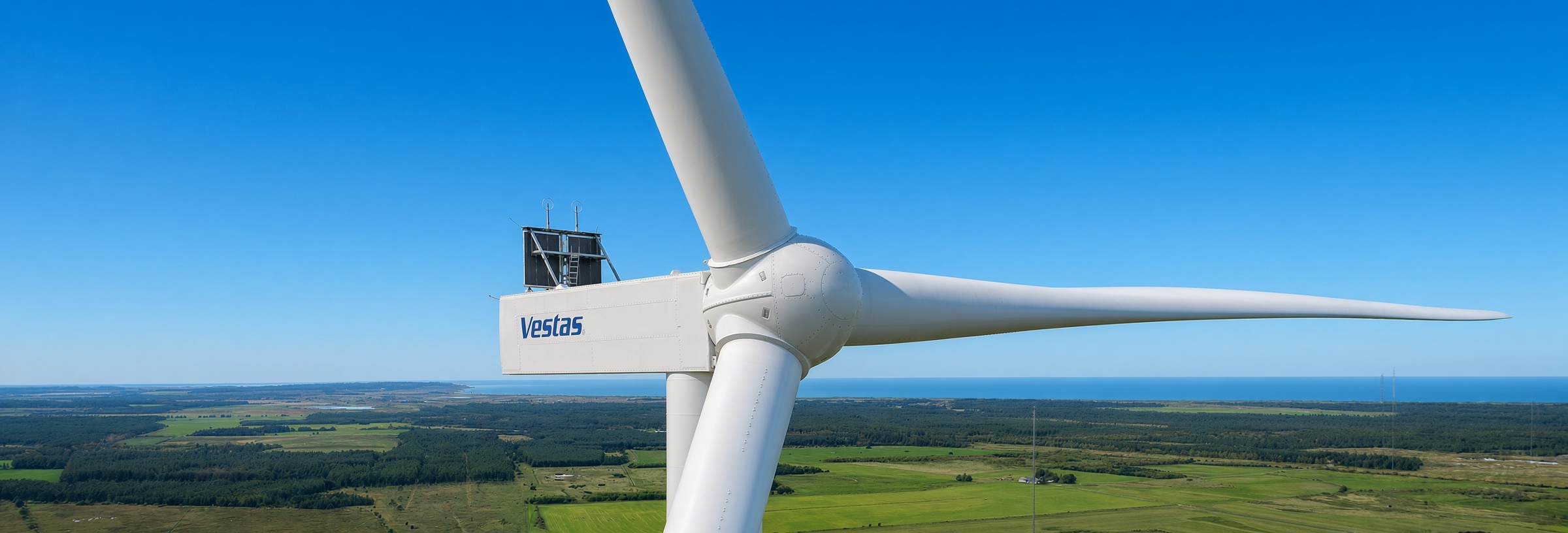 Wind turbine against a clear blue sky over a green coastal landscape